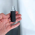 Hand holding a black and silver fluxe perfume atomizer in hand
