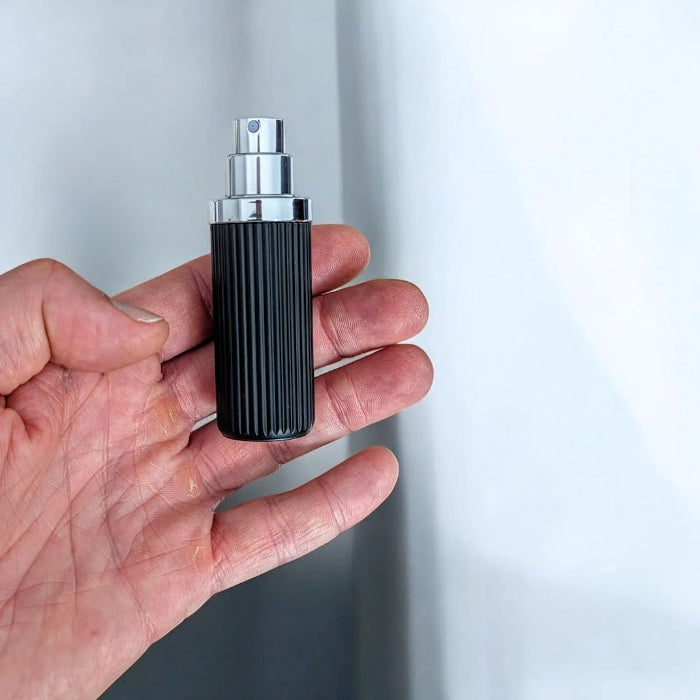 Hand holding a black and silver fluxe perfume atomizer in hand