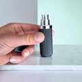 Hand holding a black and silver cylindrical perfume atomizer against a light background