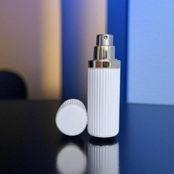 White moulded perfume atomizer with silver top on a reflective surface 
